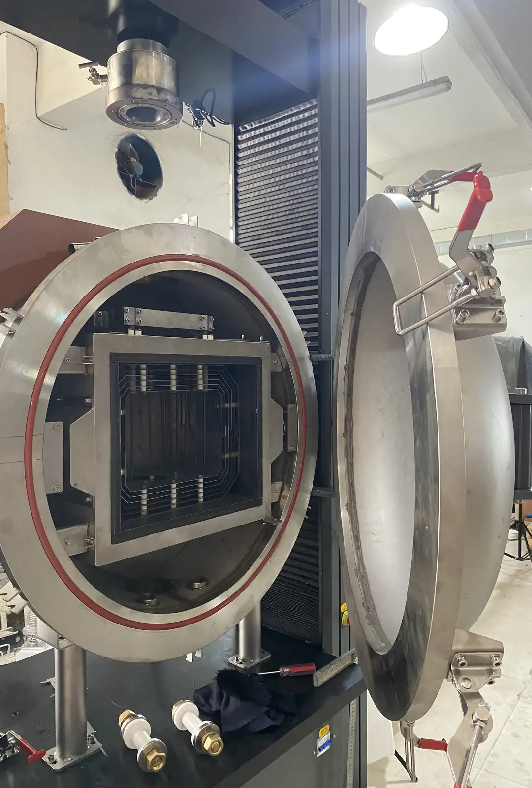 Open cylindrical vacuum hot press vessel showing the pressure frame, ram path, door seal and heated enclosure
